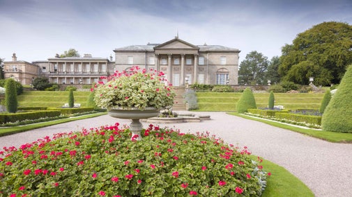 The grand front of Tatton Park, Cheshire, with red flowers in the driveway displays